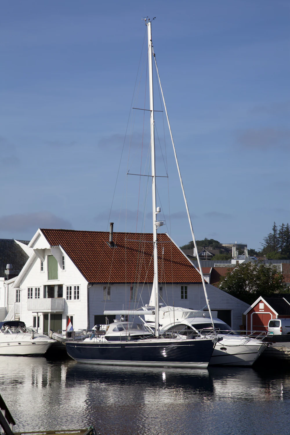 Seilbåt fortøyd ved en brygge foran et hvitt sjøhus